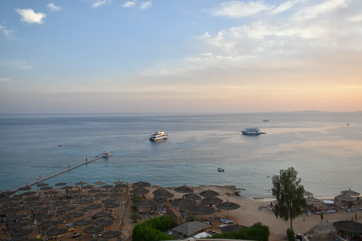 Stunning aerial view of Sharm El Sheikh's beach and sea during sunset with boats and parasols.