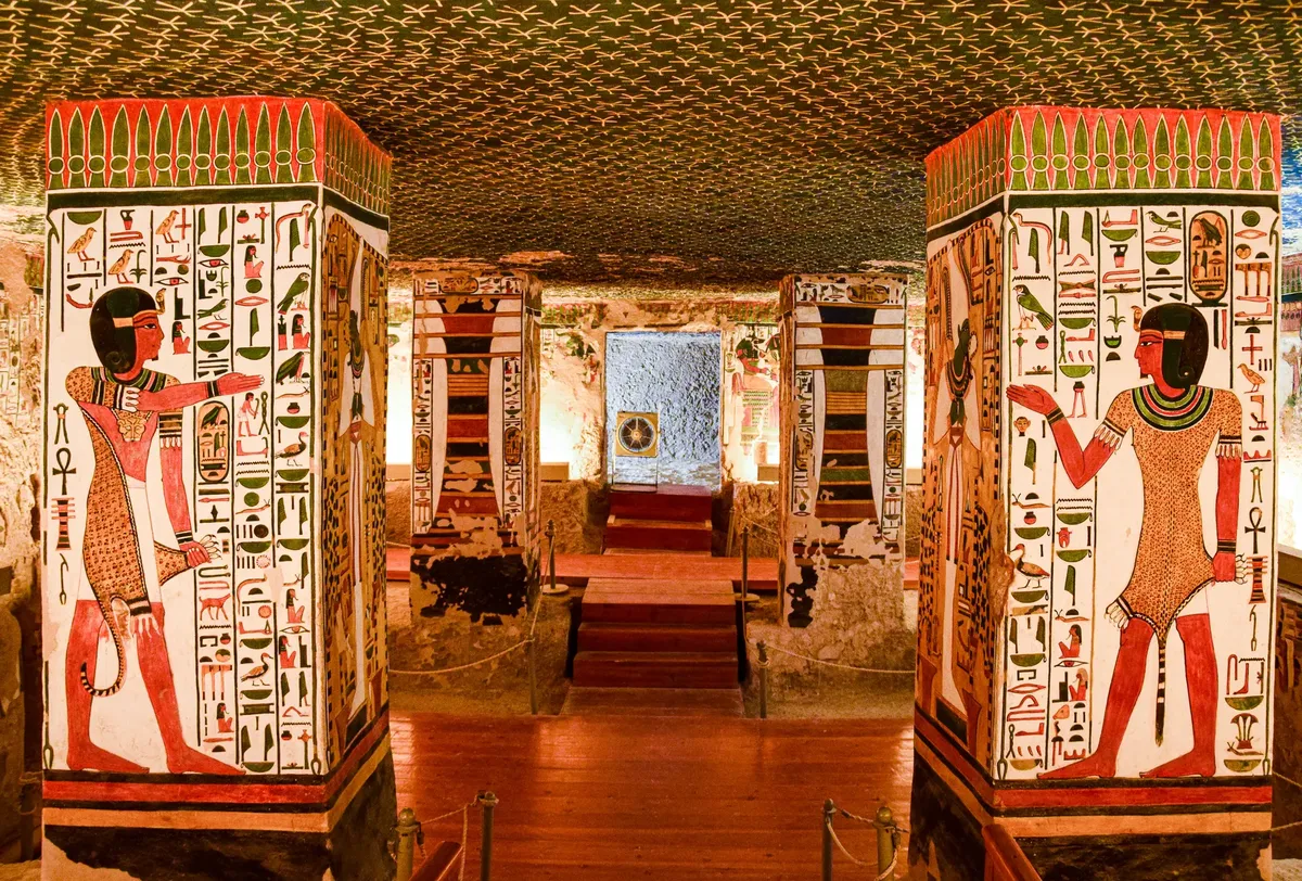 Interior of an ancient Egyptian tomb featuring vividly painted columns with hieroglyphics and murals.